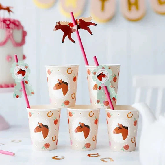 Vijf kartonnen bekers met paarden, bloemen en hoefijzers, met roze rietjes en paardendecoraties op tafel.