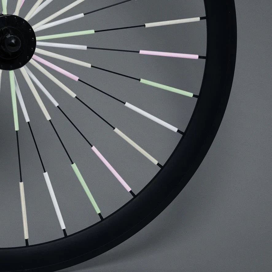 Fietswiel met Sparkle-spaakreflectoren in lichtgroen, roze en wit tegen een grijze achtergrond.