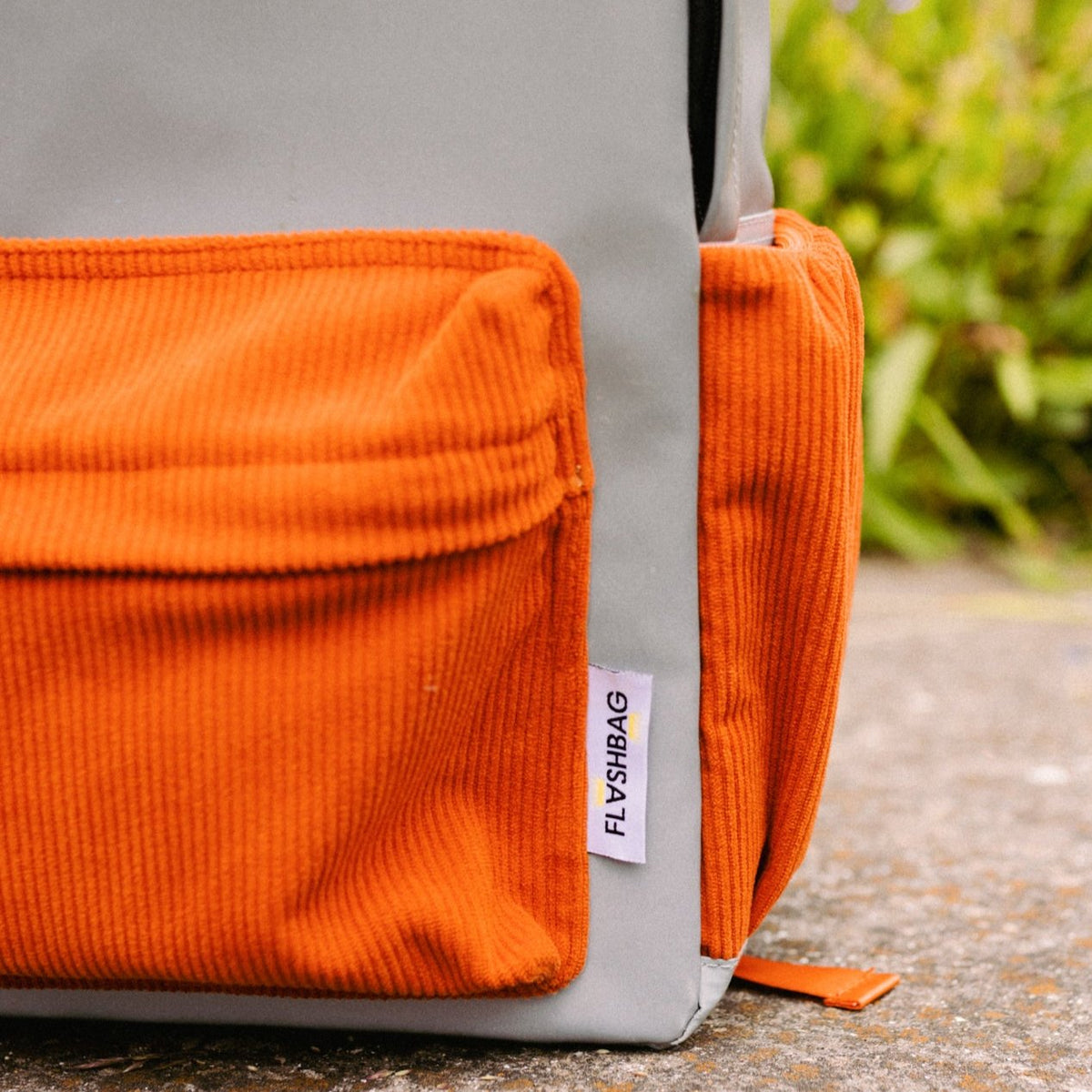 Detail van de grijze Flashbag Charlie rugzak met oranje ribfluwelen voorvak en zijvak.