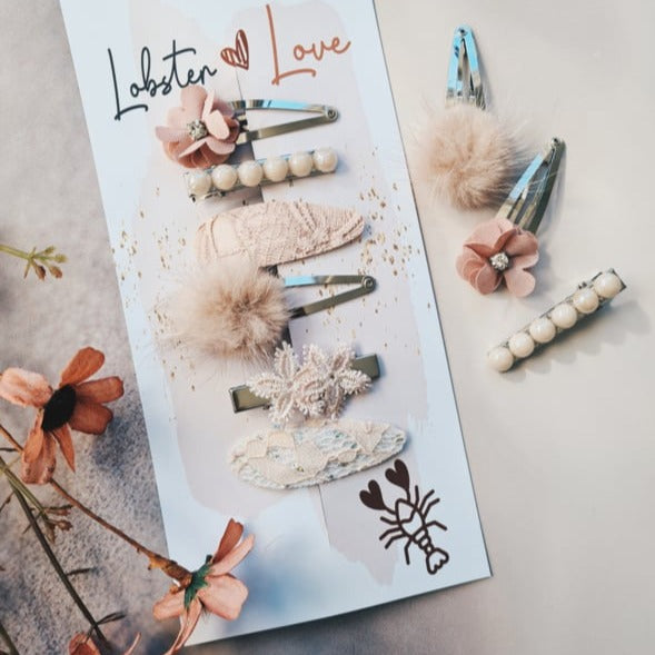Haarspeldjes Cloud Mauve in zachtroze tinten met bloemen, pareltjes, kant en pluizige details op en naast een kaart.