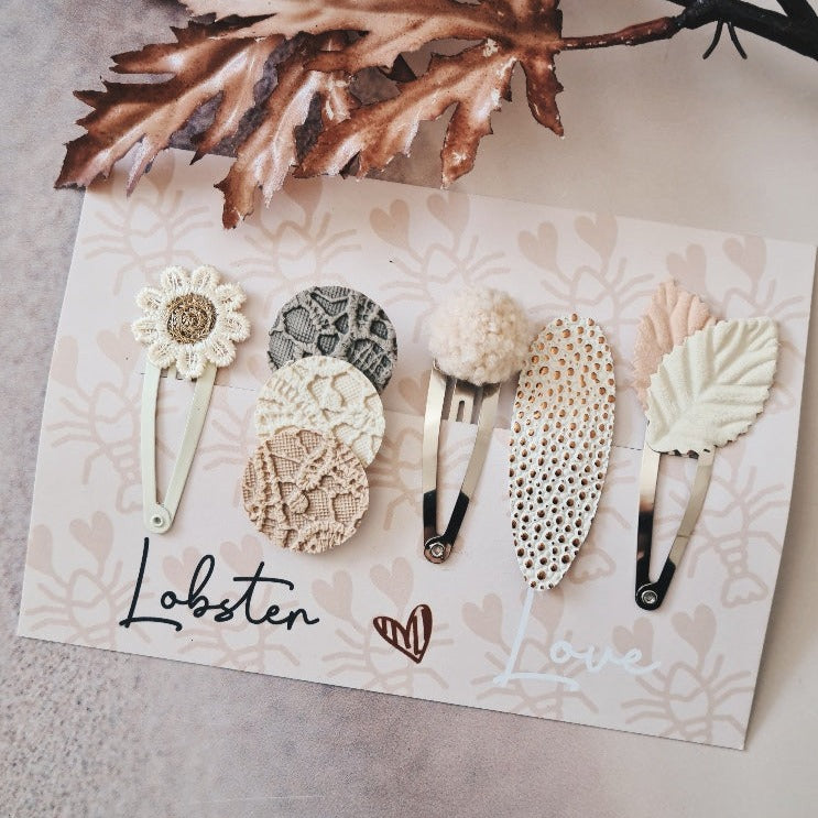Pastel Autumn haarspeldjes in nude tinten met een bloem, ronde stoffen details, een pluizig bolletje en blaadjes.