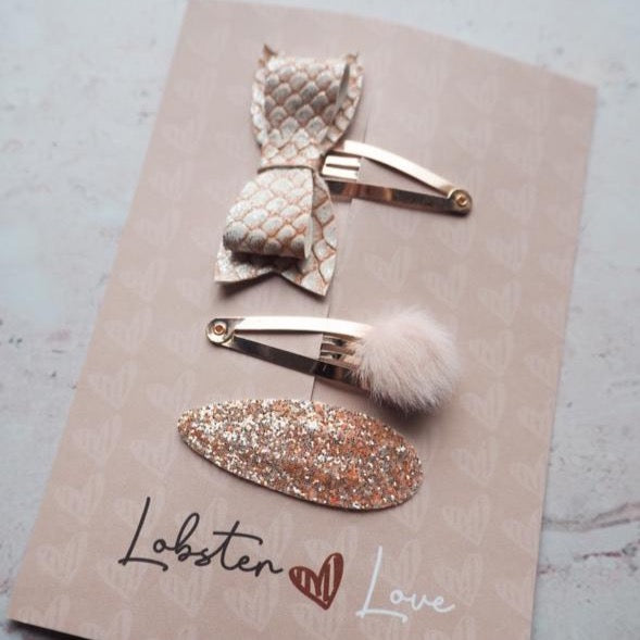 Drie zalmroze haarspeldjes op een kaartje: één met strik, één met een pluizig bolletje en één met glitters.