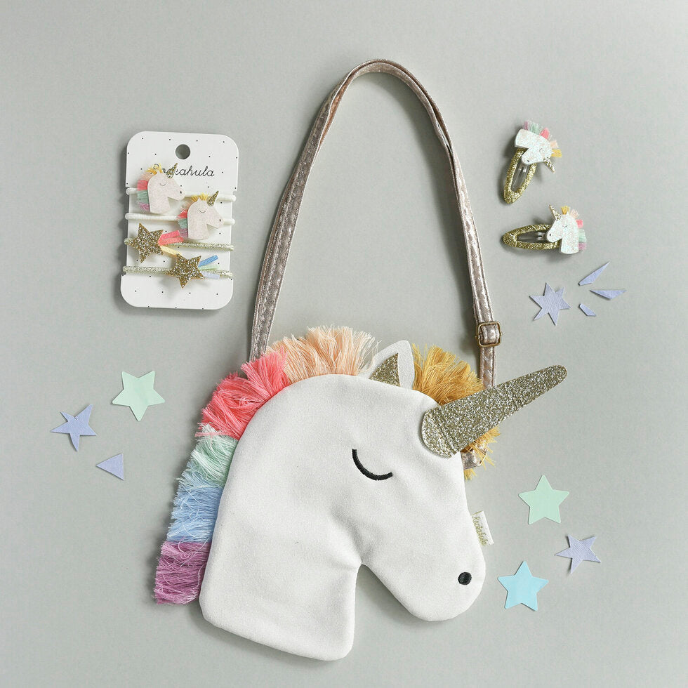 Witte eenhoornhandtas met regenboogmanen en gouden glitterhoorn, naast bijpassende haaraccessoires en losse sterren.