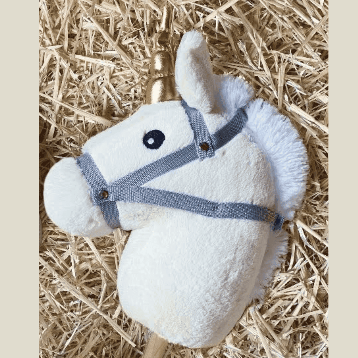 Witte kop van het Hoppy Horse Unicorn stokpaard op stro, met witte manen, grijs halster en goudkleurige hoorn.