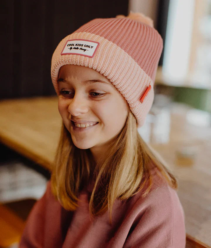 Kind draagt de roze Block Blush muts van Hello Hossy met lichtroze omslag en pompon.