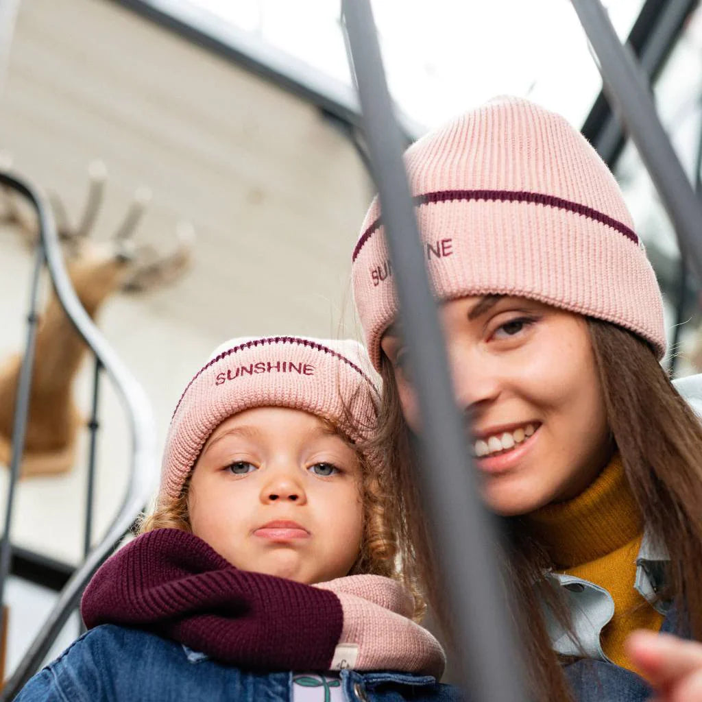 Kind en vrouw met bijpassende roze Sunshine-mutsen met pruimkleurige rand, samen bij een trap.