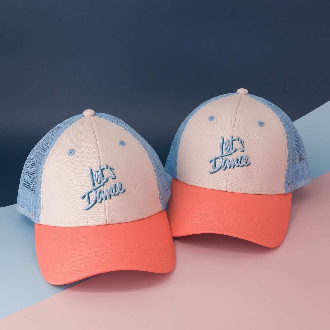 Twee Let's Dance-petten met ecru voorkant, blauw borduursel, koraalkleurige klep en lichtblauw gaas.