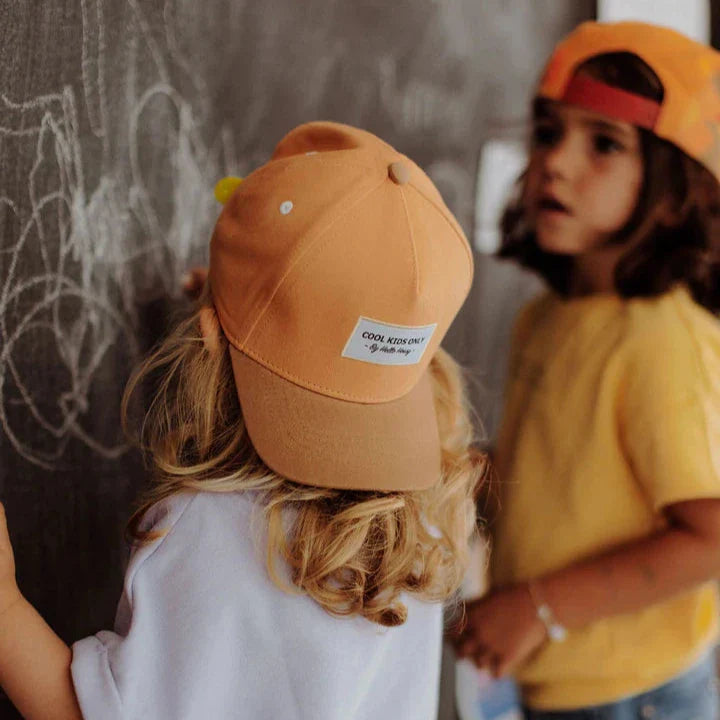 Twee kinderen bij een krijtbord, met vooraan een kind dat de Mini Tan pet achterstevoren draagt.
