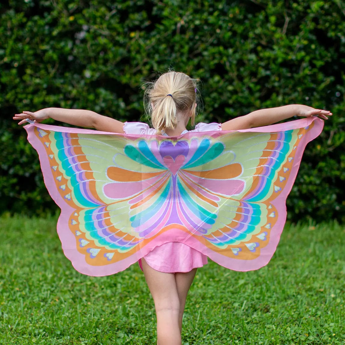 Achteraanzicht van een kind met uitgespreide vlindervleugels met regenboogpatroon en roze randen
