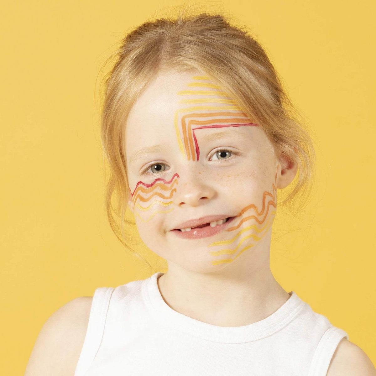 Kind met gele, oranje en rode lijnen op het gezicht tegen een gele achtergrond