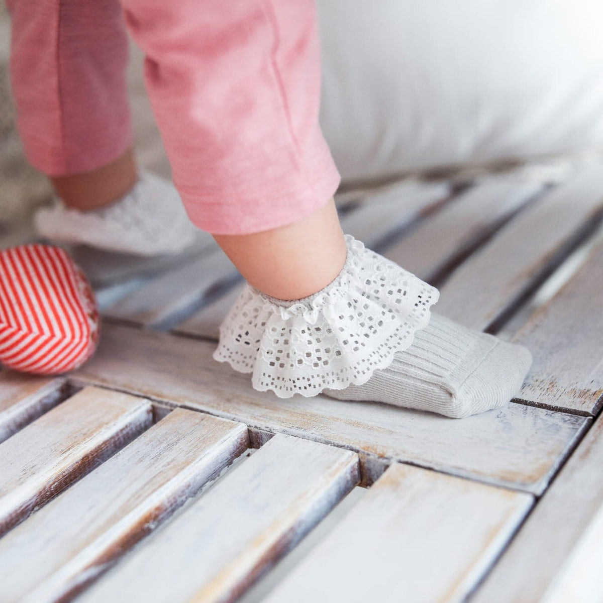 Kind met roze broek en grijze Vintage Love sokken met witte kanten boord op een houten ondergrond.