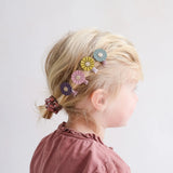 Vier Autumn Daisy mini-haarclips van Mimi & Lula met paarse, roze, gele en blauwe bloemen in het blonde haar van een kind.