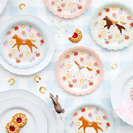 Kartonnen bordjes met paarden, bloemen en gouden hoefijzers, met pastelroze en lichtblauwe randen op een gedekte tafel.
