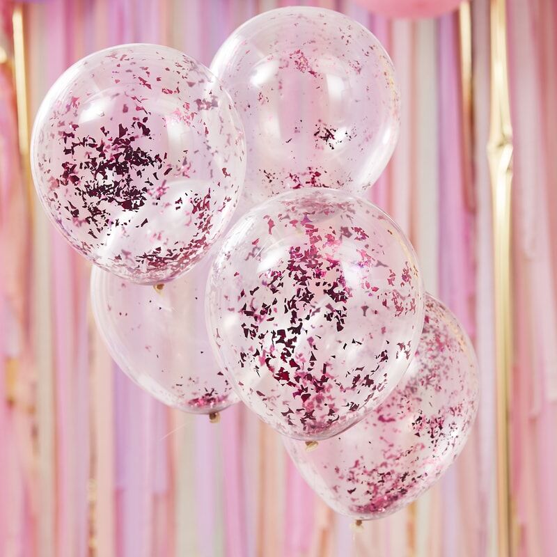 Vijf transparante ballonnen met roze confetti voor een achtergrond van roze en goudkleurige slingers.