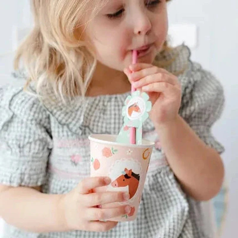 Kind drinkt met een roze rietje uit een kartonnen beker met paardenprint, bloemen en hoefijzers.