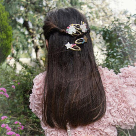 Eenhoornhaarclips en stervormige glitterclips in lang donker haar, bij een roze jas met bloemenstructuur.