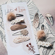 Collared Dove haarspeldjes met beige pompons, bloemen, luipaardprint en een bruin geweven speldje op een kaart.