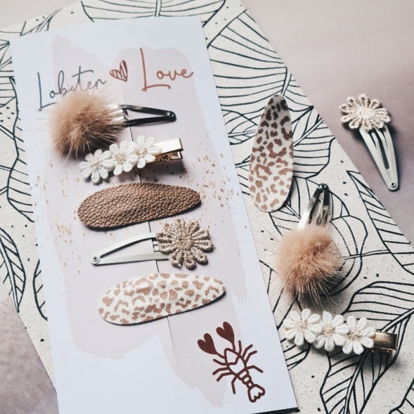 Collared Dove haarspeldjes met beige pompons, bloemen, luipaardprint en een bruin geweven speldje op een kaart.