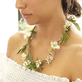 Detail van een bloemenketting met witte en lichtroze bloemen en groene bladeren, gedragen rond de hals.