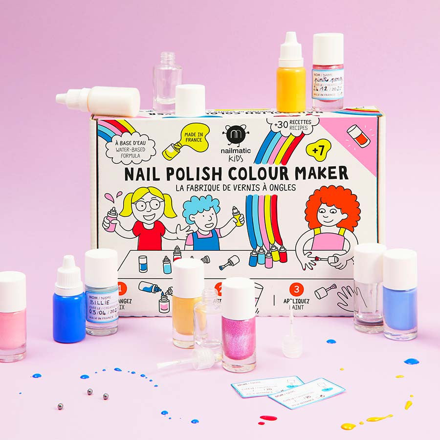 Nailmatic DIY-nagellakset met gekleurde flesjes en glitters rond de doos op een roze achtergrond.