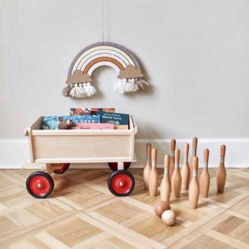 DIY regenboog Nude aan de muur boven een speelgoedwagen met boeken, naast houten kegels en ballen.