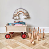 DIY regenboog Nude aan de muur boven een speelgoedwagen met boeken, naast houten kegels en ballen.