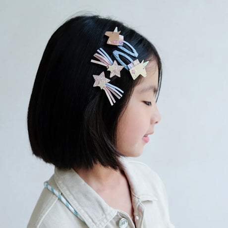 Kind met vier haarclips in donker haar: twee eenhoorns en twee glinsterende vallende sterren met pastelkleurige linten.