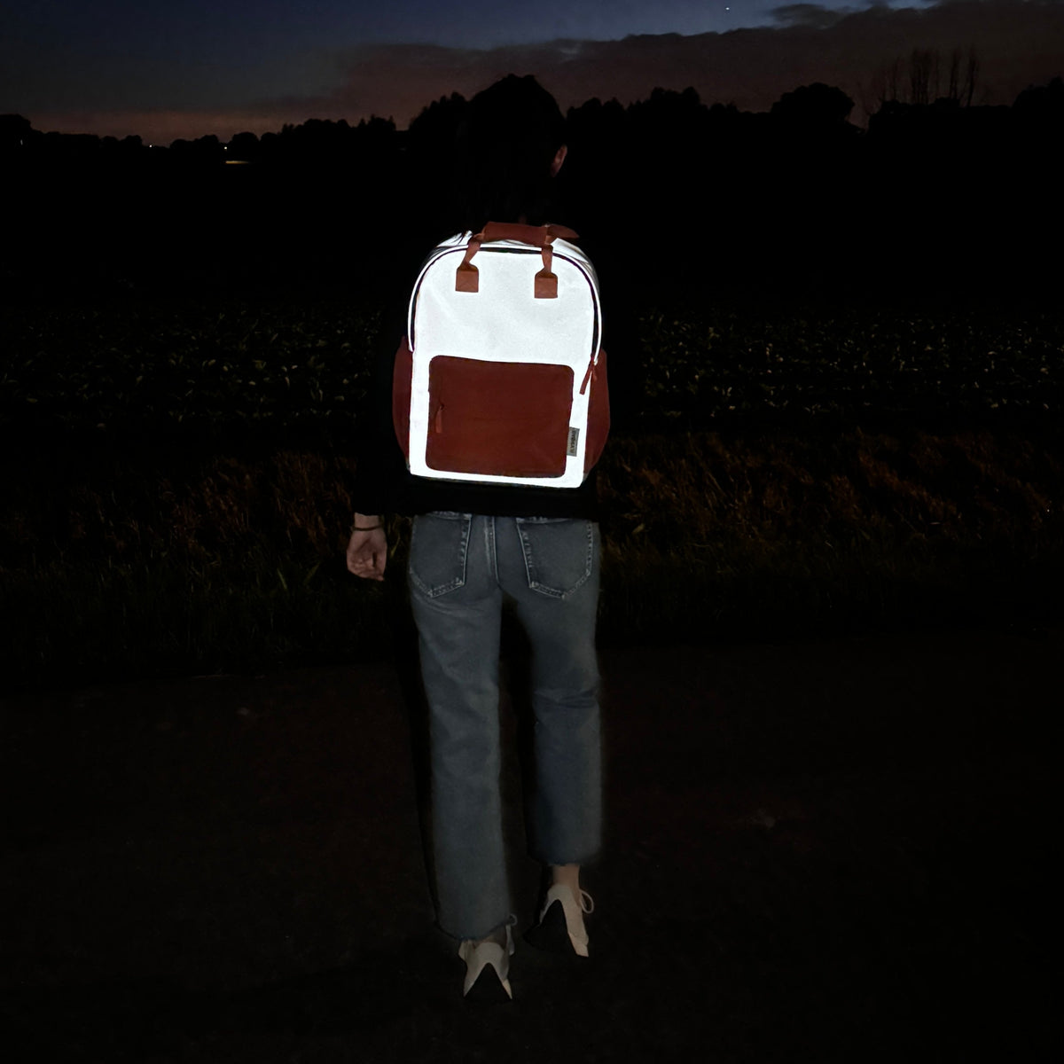Flashbag Charlie rugzak op de rug van een persoon in het donker, met fel oplichtende reflecterende stof.