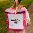 Kind draagt de roze Flashbag Lou-rugzak met grijs reflecterend voorpaneel en de tekst 'watch me' op een pad.