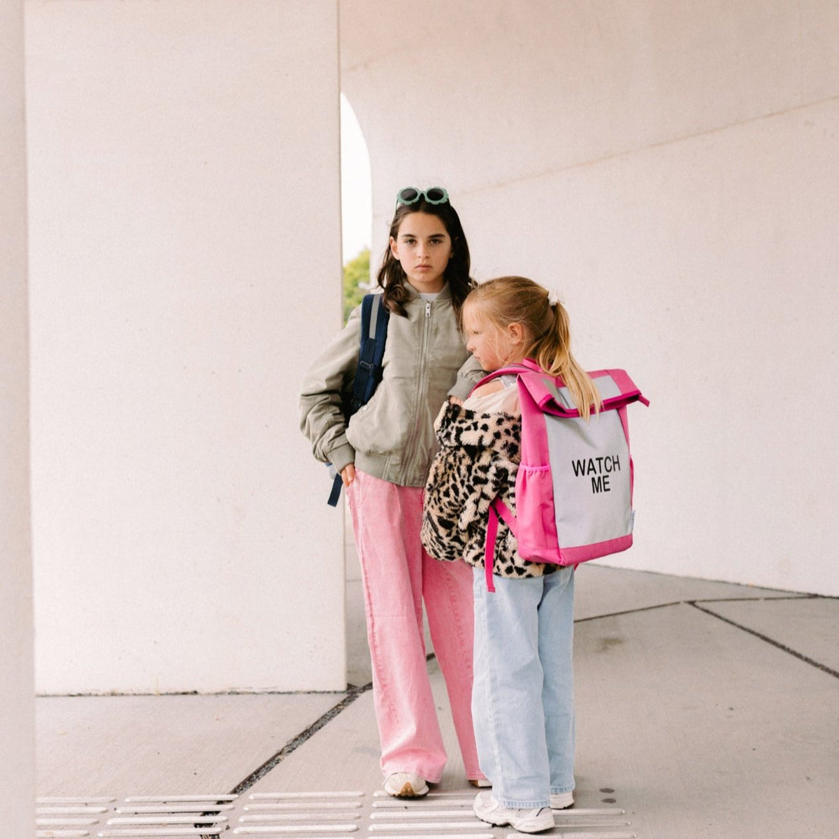 Meisje draagt de roze Flashbag Lou-rugzak met grijs voorpaneel naast een ander meisje.