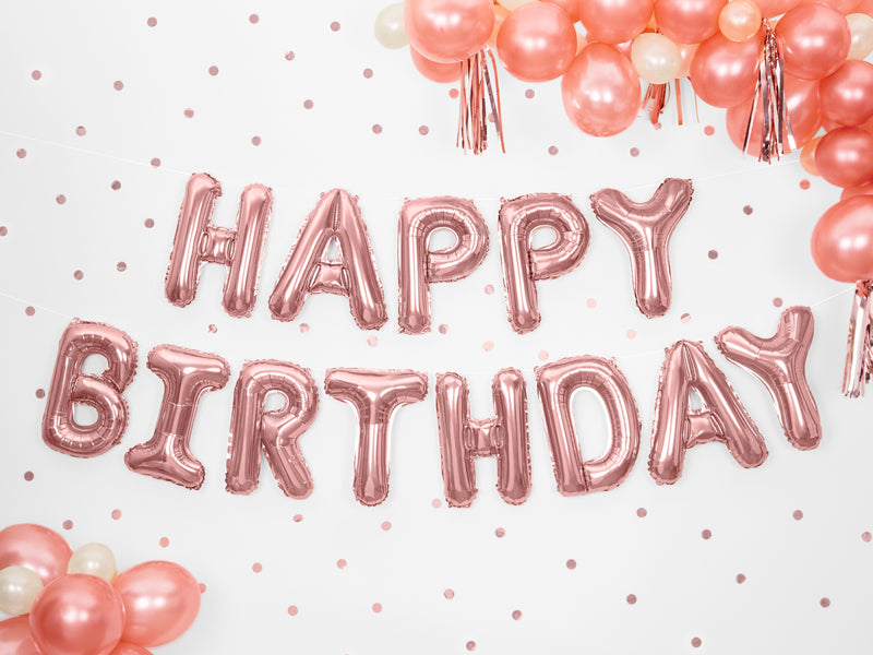 Roségouden Happy Birthday-folieballonnen aan een muur met stippen, omringd door roze en witte ballonnen