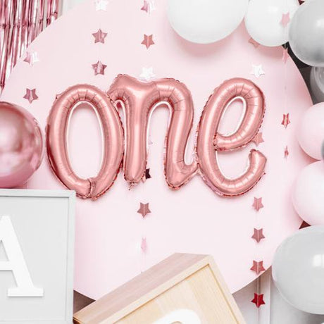 Roségouden folieballon met het woord 'one' tegen een roze achtergrond met sterren en ballonnen.