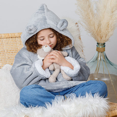 Kind in een grijze beer hoodie plaid met oortjes aan de capuchon, zittend met een knuffelbeer.