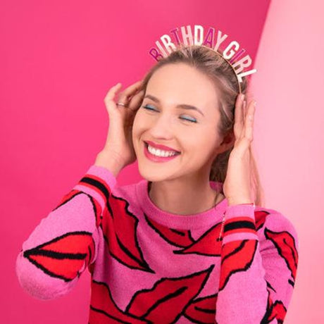 Vrouw draagt de haarband ‘Birthday Girl’ met roze en witte letters tegen een roze achtergrond.