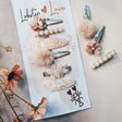 Haarspeldjes Cloud Mauve in zachtroze tinten met bloemen, pareltjes, kant en pluizige details op en naast een kaart.