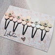 Vijf zwarte haarspeldjes op een kaart, met pastelkleurige bloemen, kraaltjes en een strasssteentje in het hart.