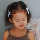Meisje met lila haarspeldjes Twist en Strik met witte strikjes aan weerszijden van haar haar.