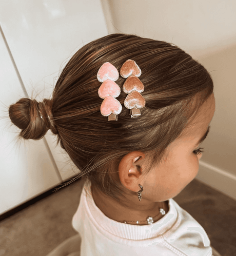 Twee haarspeldjes met roze en oudroze velvet hartjes in het opgestoken haar van een meisje