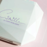 Camille highlighter in een gesloten, wit diamantvormig doosje met paars logo op een roze achtergrond.