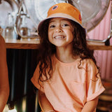 Lachend kind met het oranje hoedje Mini Orange van Hello Hossy en een perzikkleurig T-shirt.