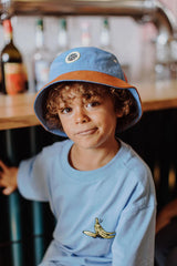 Kind met het lichtblauwe hoedje Mini Yosemite met roestbruine rand en een lichtblauw T-shirt.