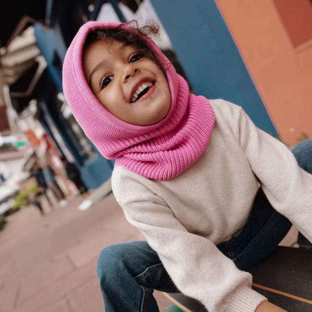 Lachend kind met roze Hoody Lila van Hello Hossy, zittend op een bankje buiten.