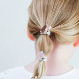 Detail van haarelastiekjes met een bruin paard en roze bloem met glinsterend hart in blond haar.