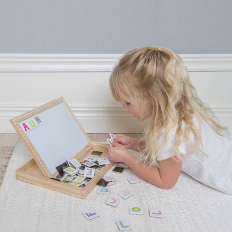 Kind ligt op de buik en speelt met de houten cijfers- en lettersmagneetpuzzel, met losse magneten op het kleed.