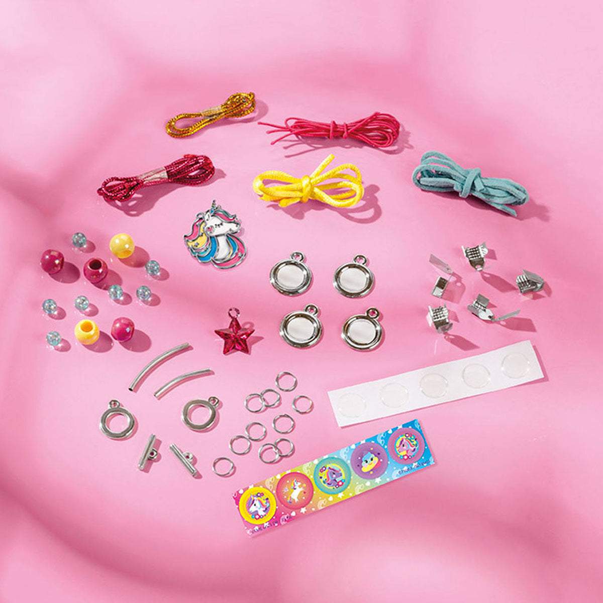 Inhoud van de Unicorn juwelenset met gekleurde koordjes, kralen, bedels, sluitingen en stickers op een roze ondergrond.