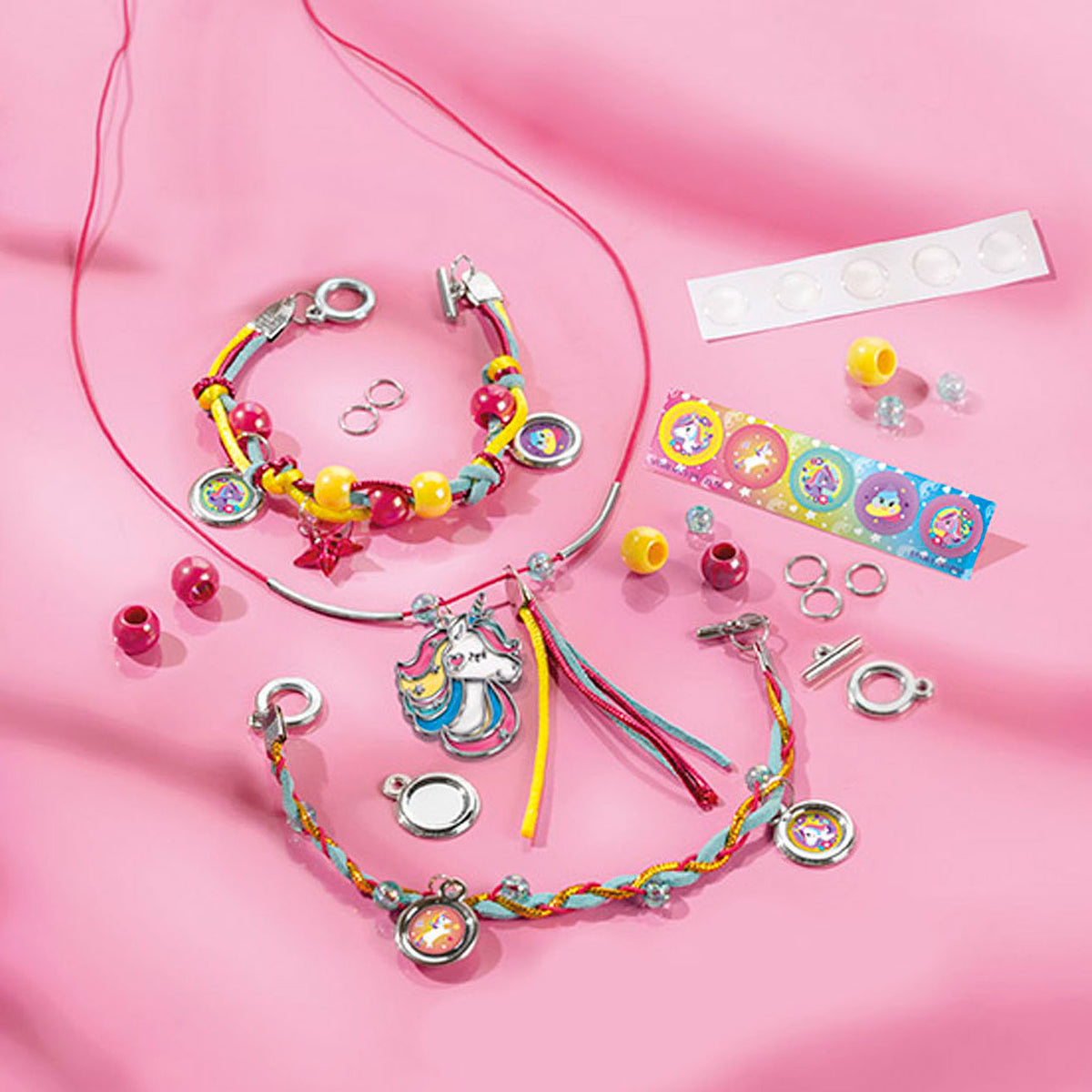 Armbandjes en een ketting met eenhoornbedel uit de Unicorn juwelenset, naast losse kralen en stickers op roze.