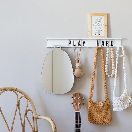 Witte magnetische kapstok met zwarte letters ‘play hard’, met een spiegel, kralenketting en gehaakte tasjes aan de haken.