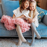 Twee meisjes op een blauwe bank met maillot Clara in crème en grijs onder hun feestelijke jurken.