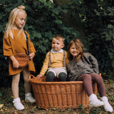 Kind met maillot Classic in Blueberry en witte schoenen op de rand van een rieten mand, naast twee andere kinderen.