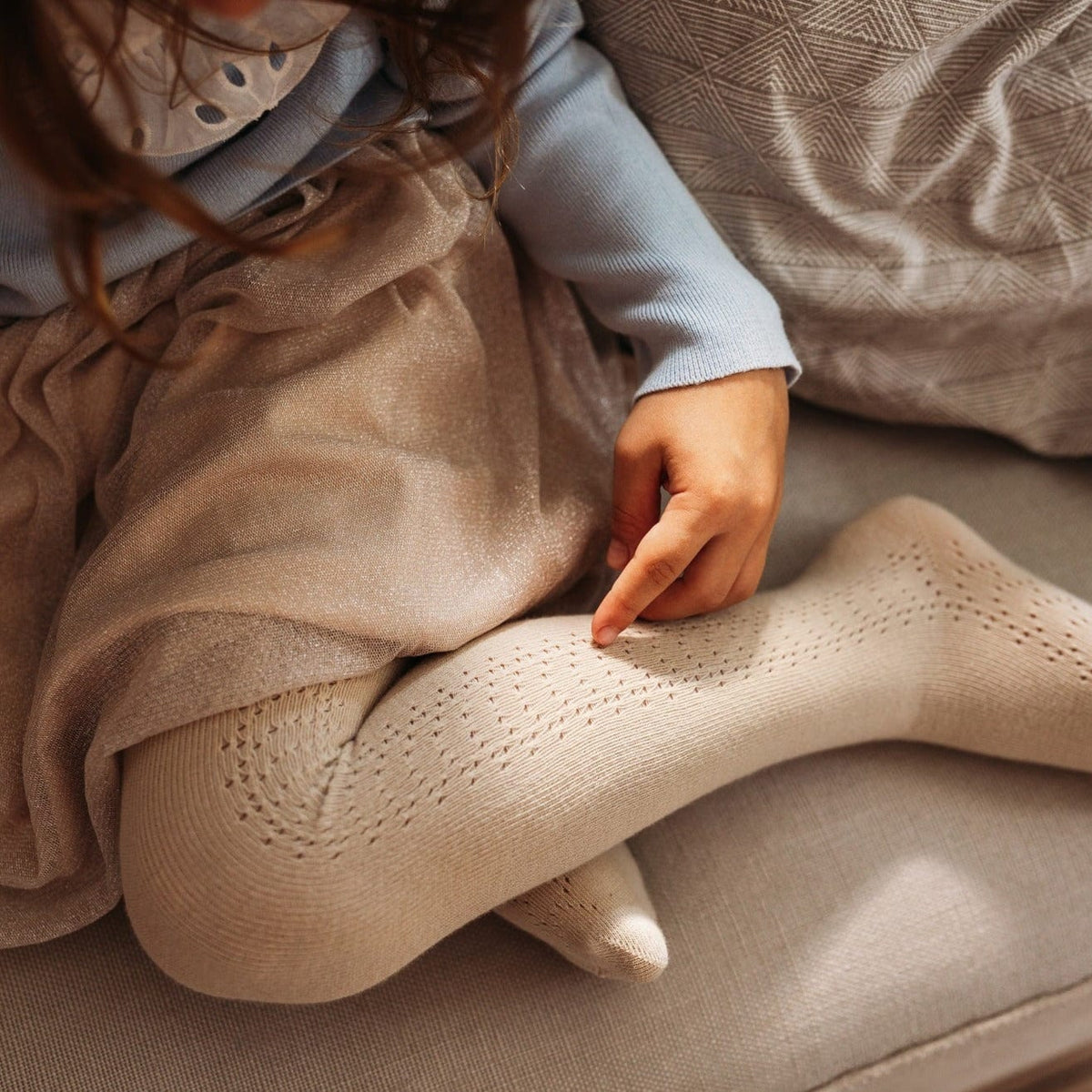 Detail van de beige maillot Josephine met fijn zijpatroon, gedragen onder een rok door een kind op de bank.